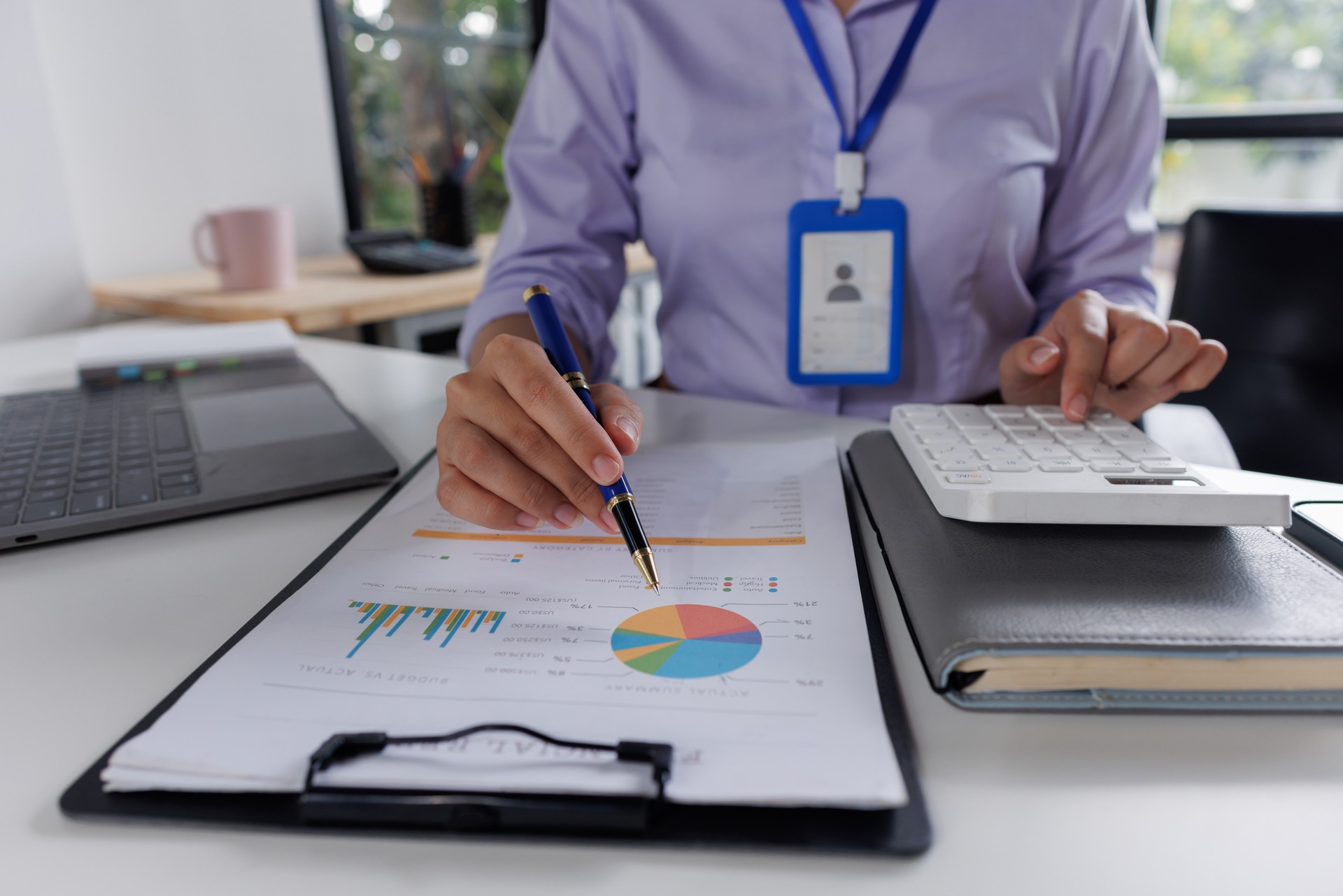 Close up of business woman or accountant hand holding pen working on calculator to calculate business data, accountancy document and laptop computer at office, business concept